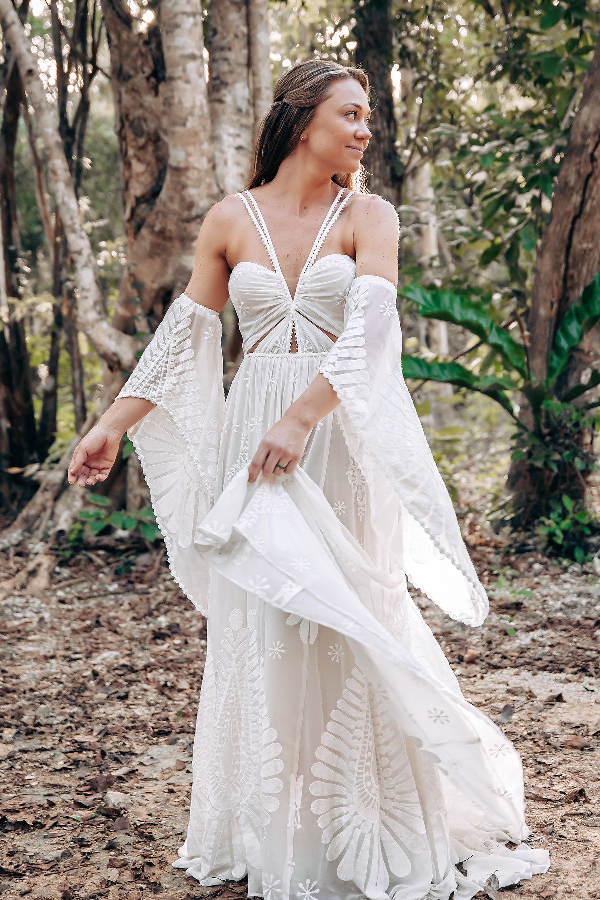 A flowing white bohemian dress with ruffled sleeves twirls gracefully in a forest setting.