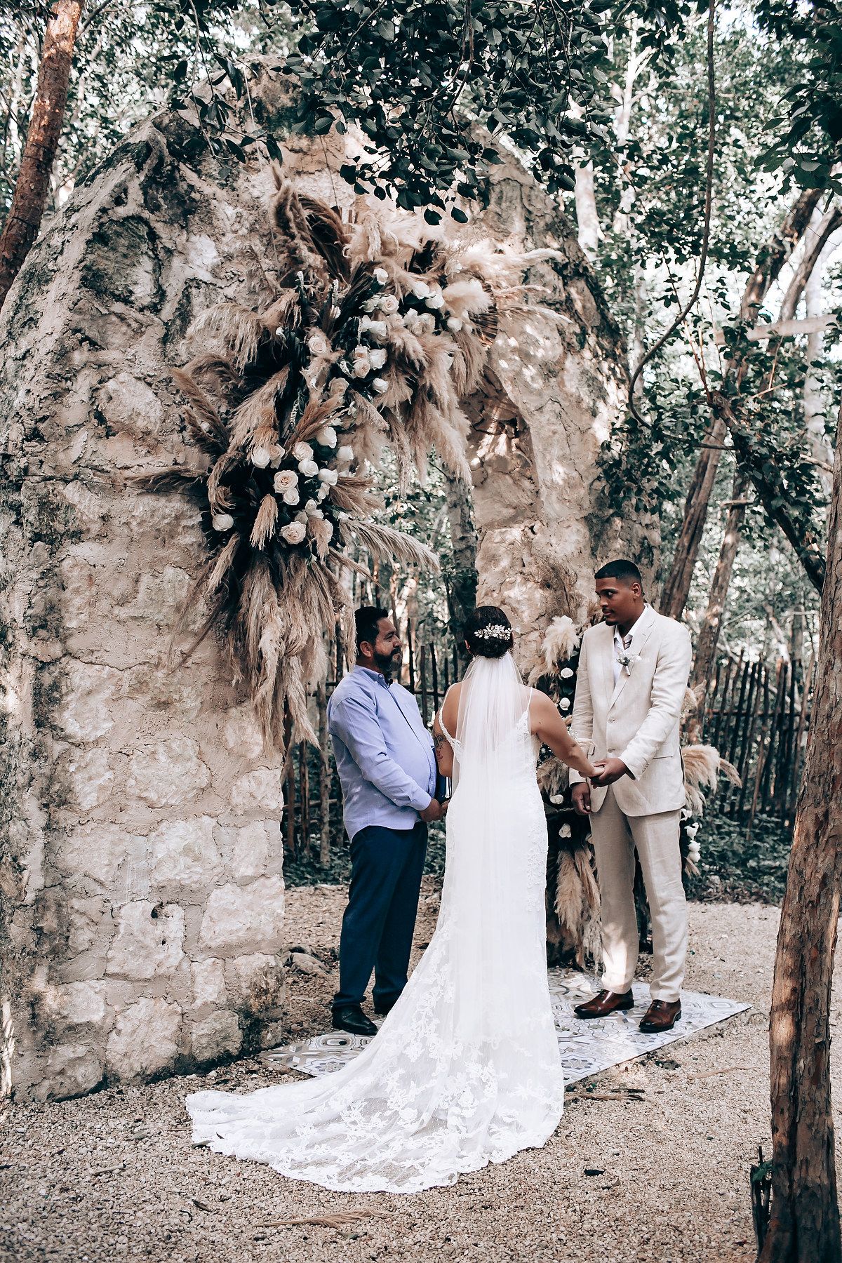 A romantic wedding couple shares intimate moments in a wooded outdoor setting with trailing white dress details.