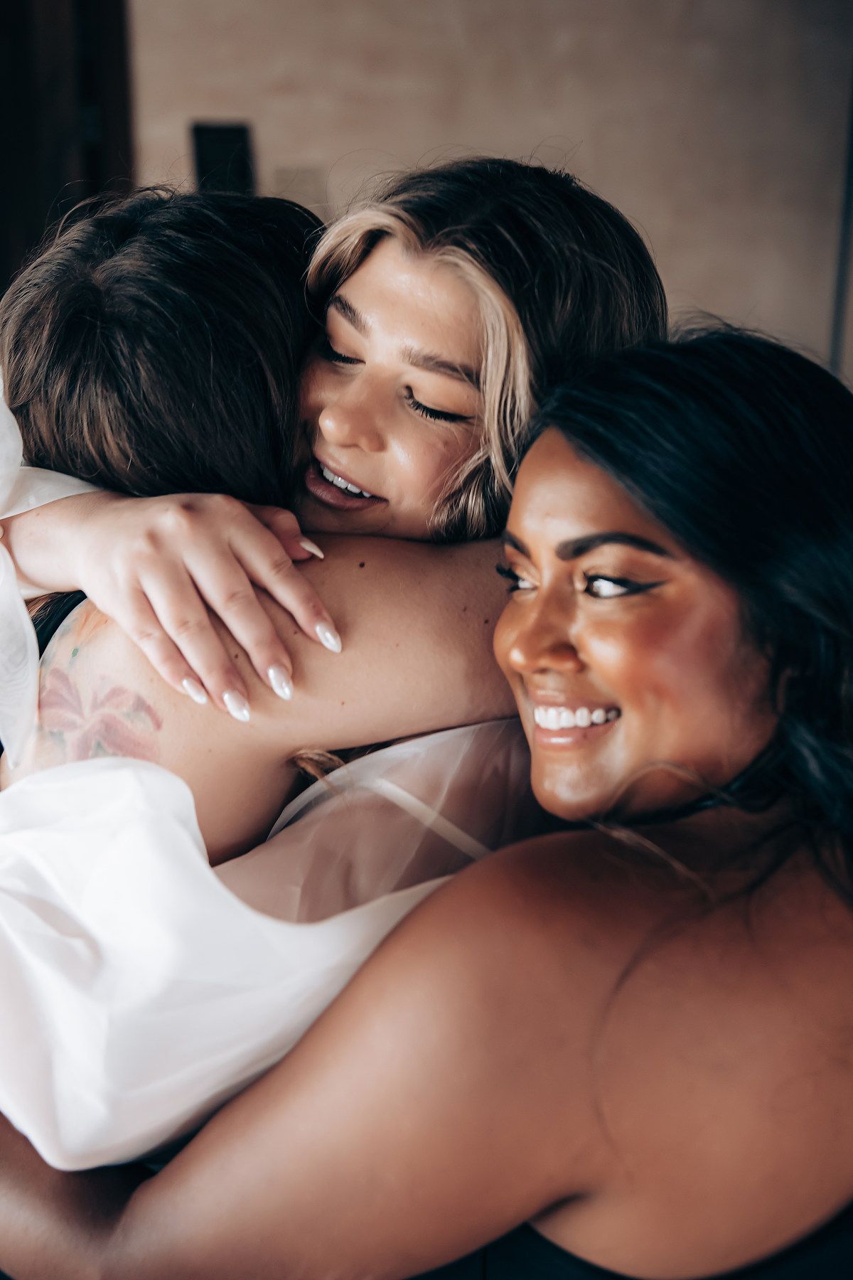 Friends sharing emotional embrace in white dresses during special moment.