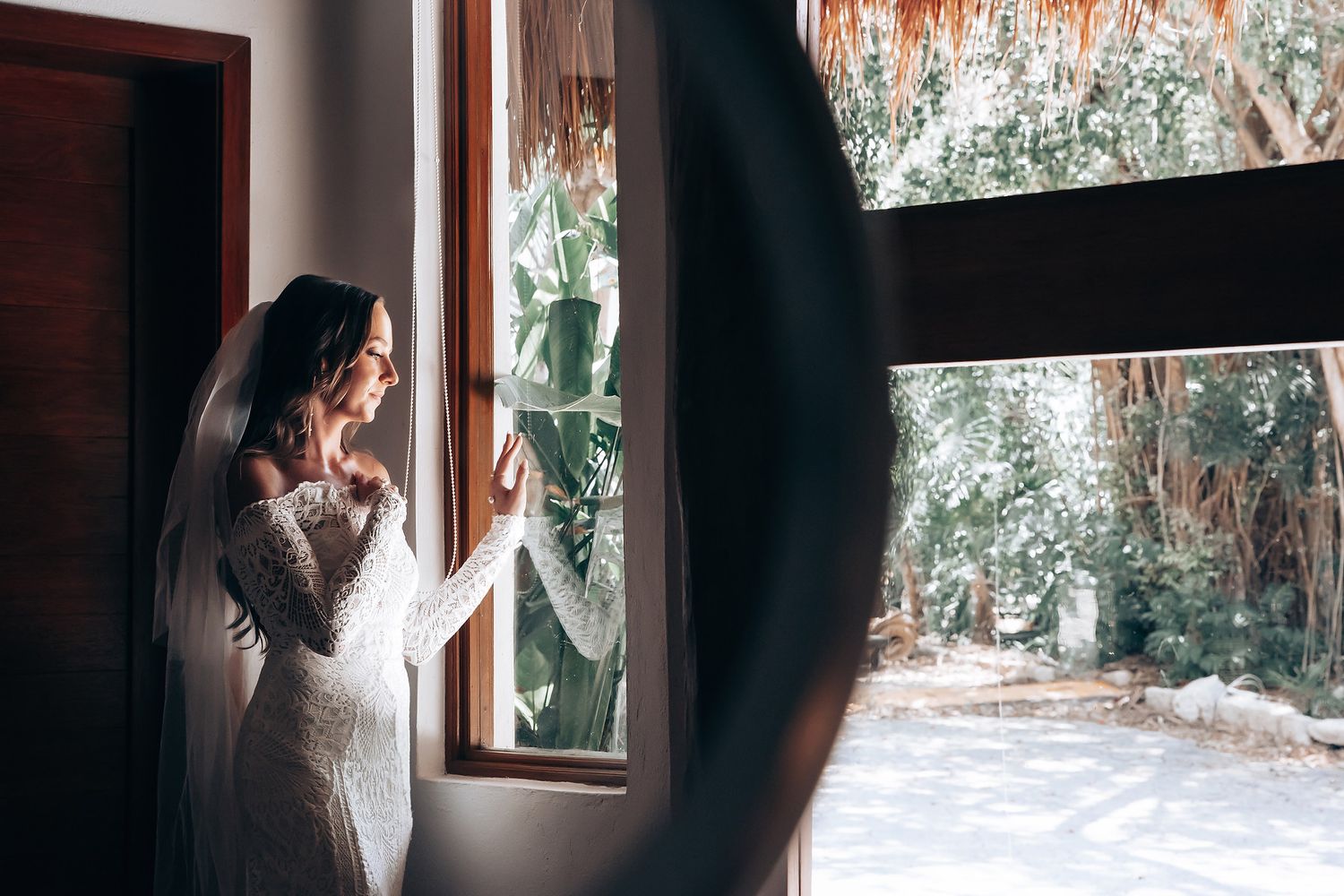 Person in white dress standing by window with natural light streaming in, creating atmospheric morning ambiance.