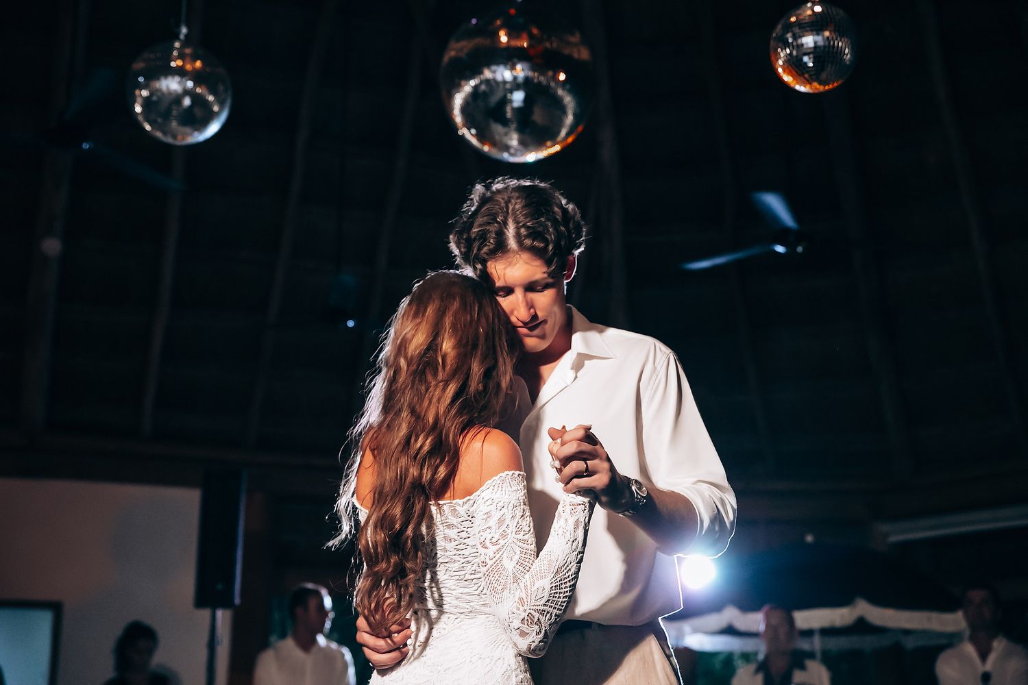 A couple shares their first dance under hanging disco balls at a dimly lit wedding reception.
