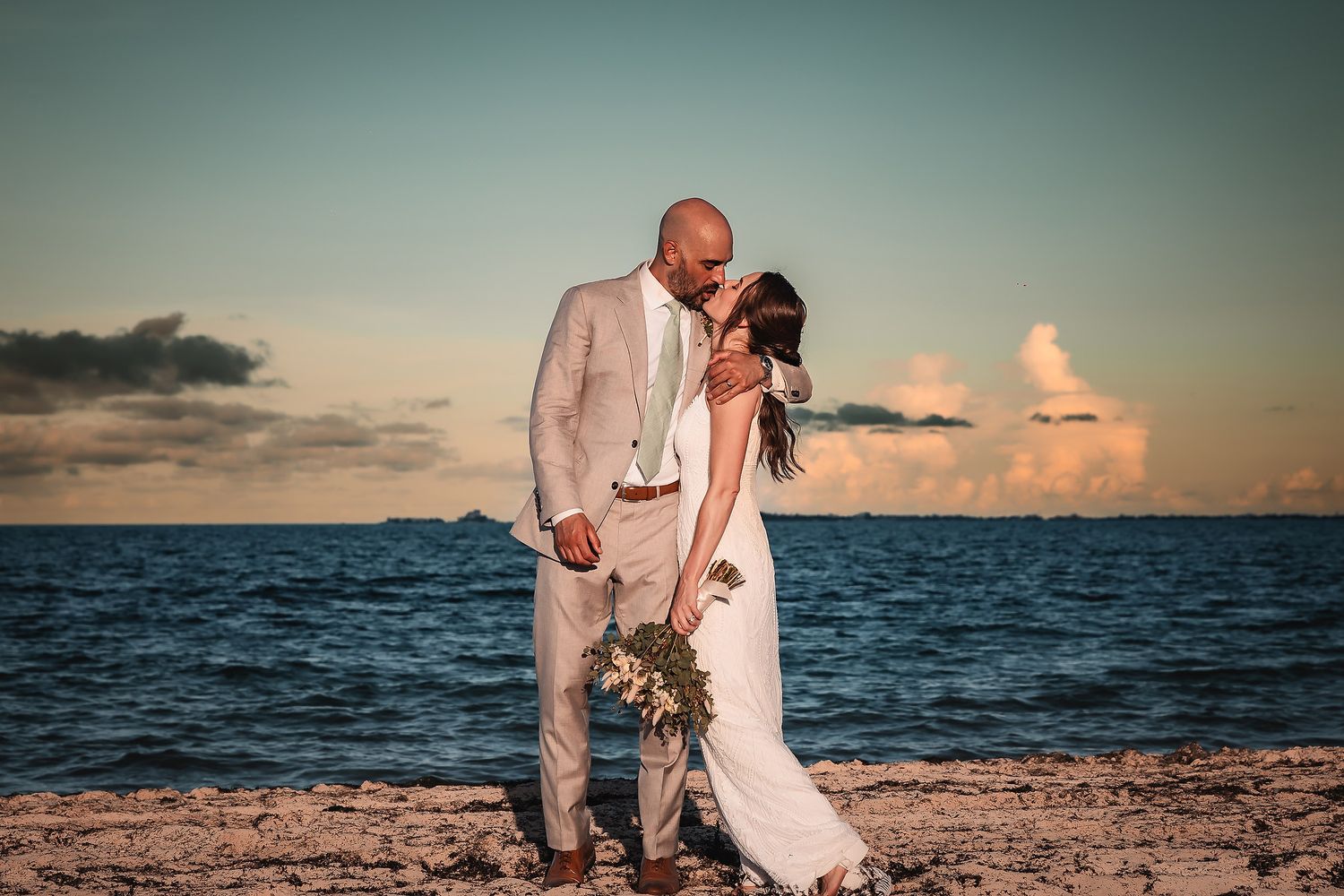 Couple sharing an intimate moment on sandy beach during golden hour with ocean waves in background.