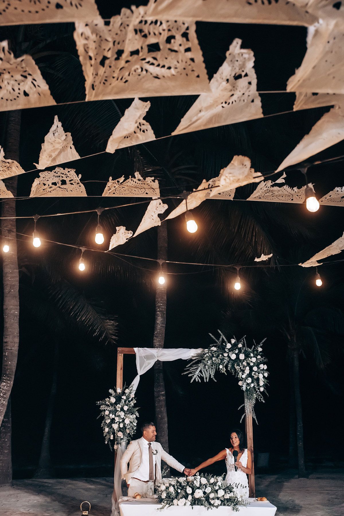 Romantic outdoor evening reception with string lights and white papel picado decorations.