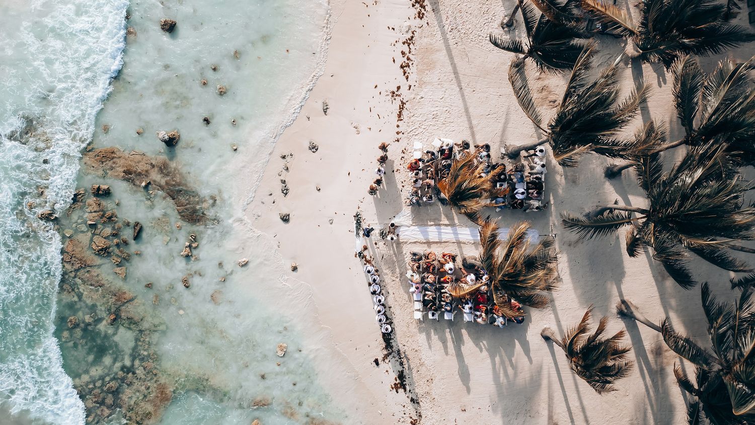 Aerial view of a beach wedding setup with palm trees and decorative elements.