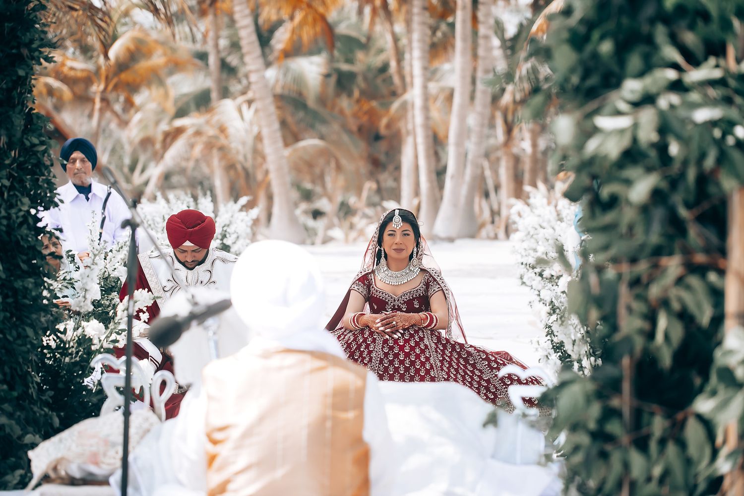 Elegant beach wedding decor with white floral arrangements and palm trees against a bright sky.