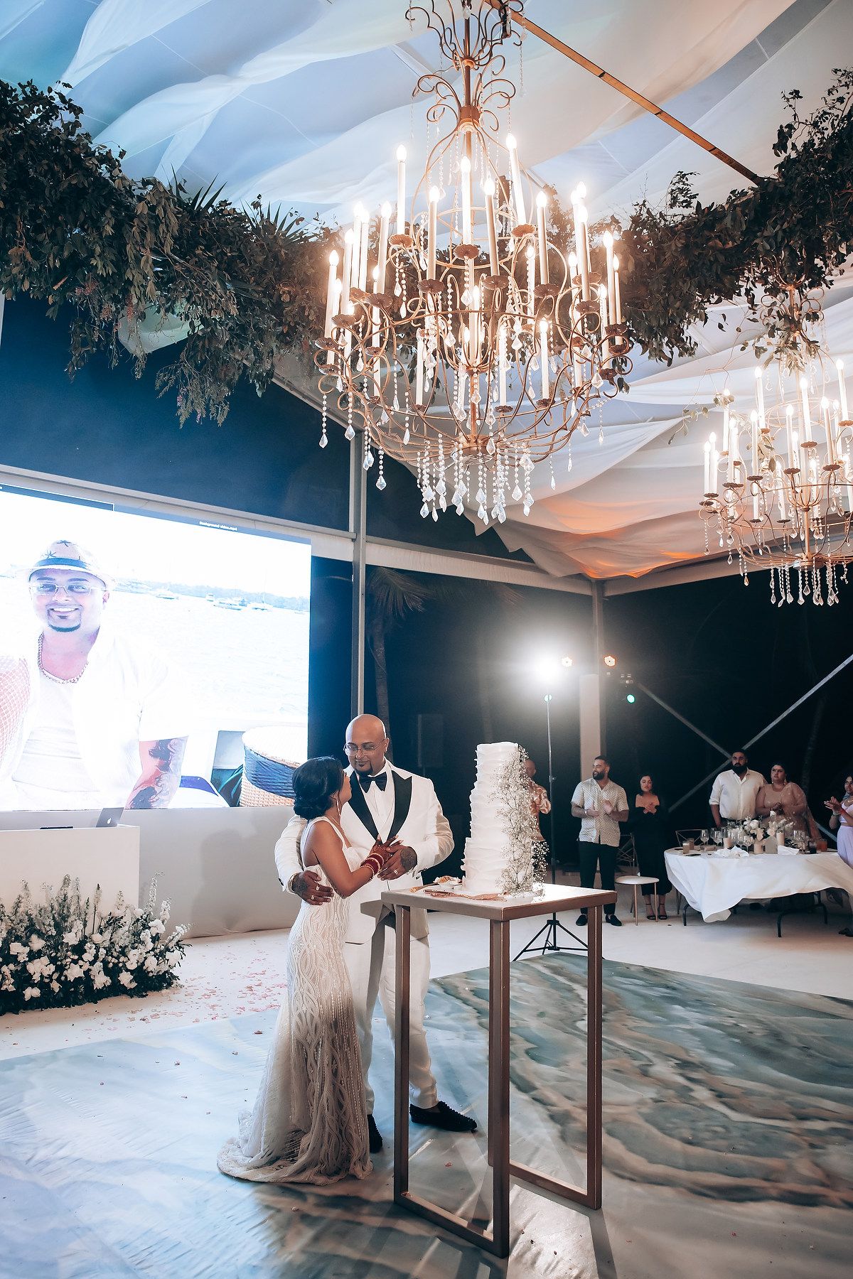Modern wedding reception setup with crystal chandeliers and elegant white decor.