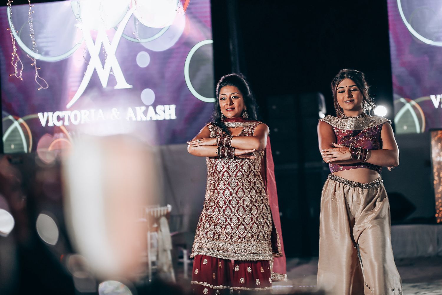 Fashion models walk the runway in elegant evening wear during a dimly lit fashion show presentation.