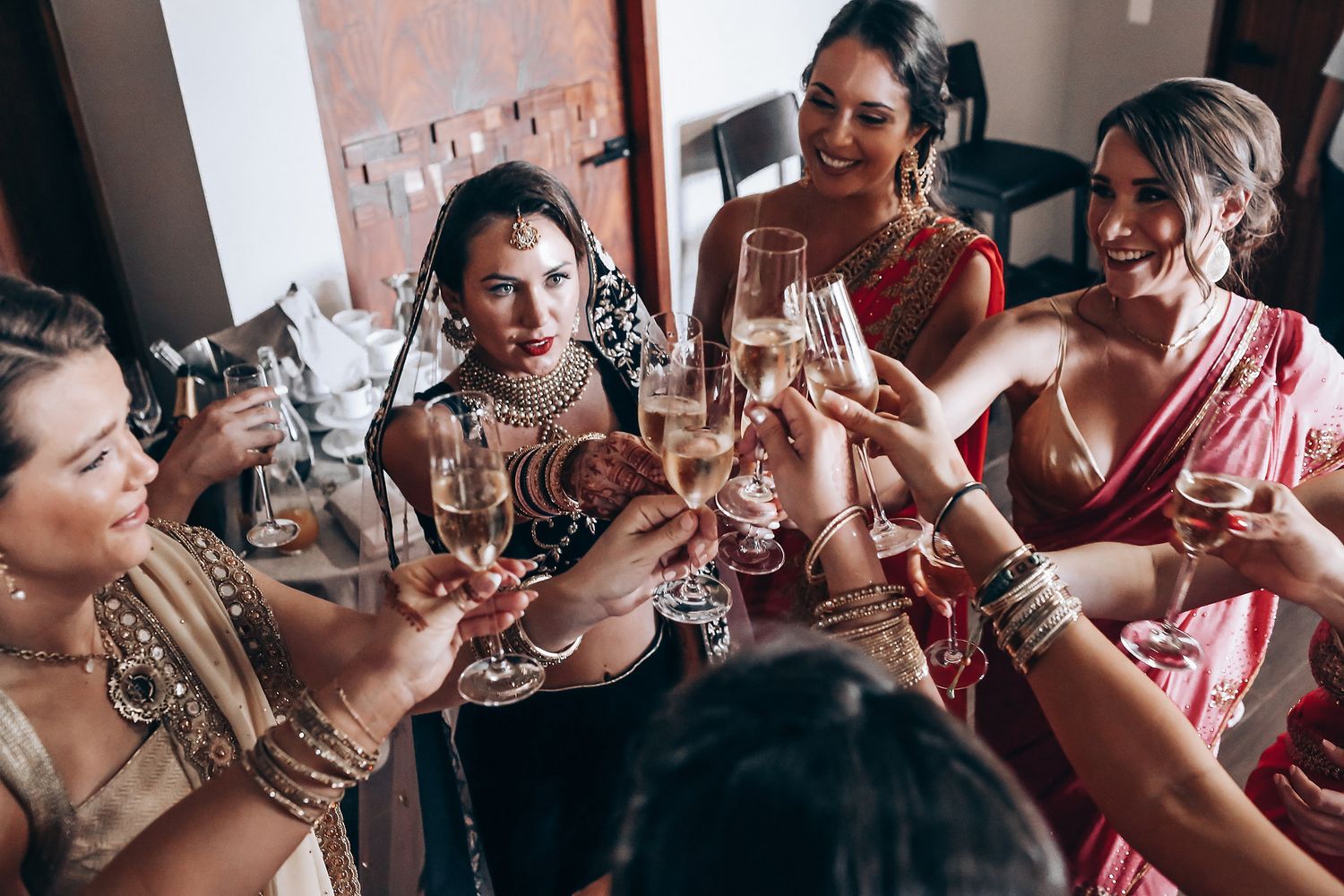 A group of people in formal attire raise their glasses in a celebratory toast at an indoor gathering.