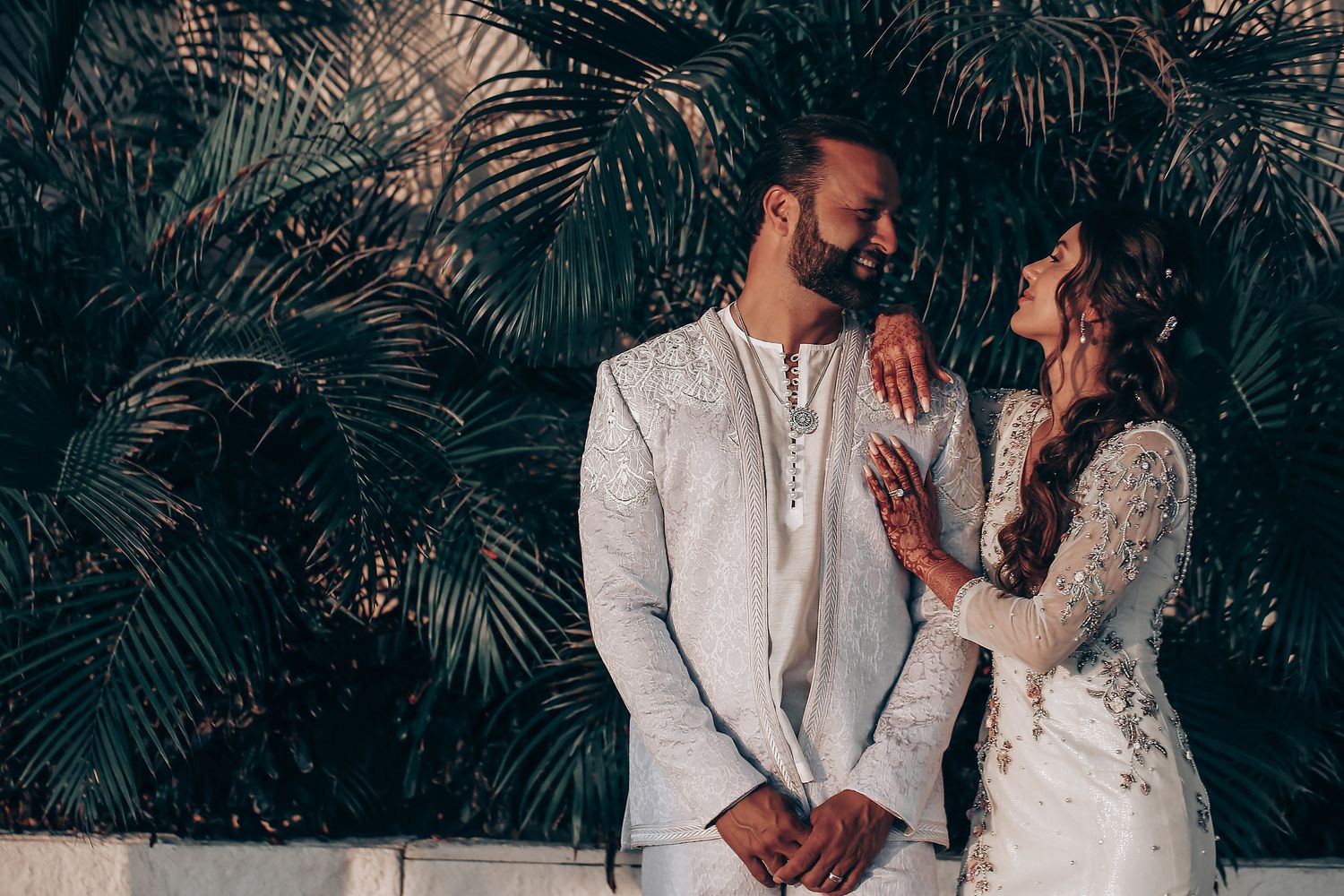 A couple shares romantic moments in front of tropical palm leaves during a wedding photoshoot.