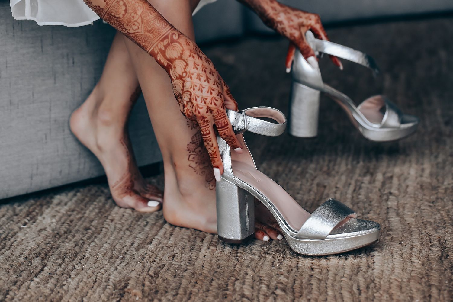 Close-up shots showing hands fastening silver metallic ankle strap sandals with block heels on carpet.