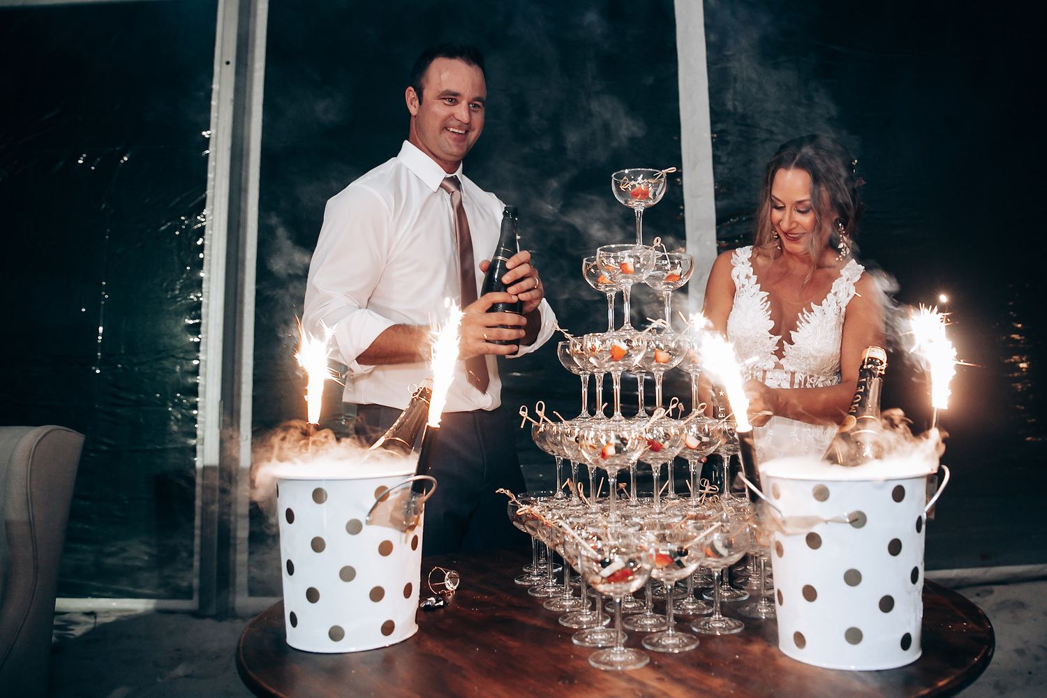 Wedding reception celebration with champagne tower and sparklers glowing in the dark elegant setting.