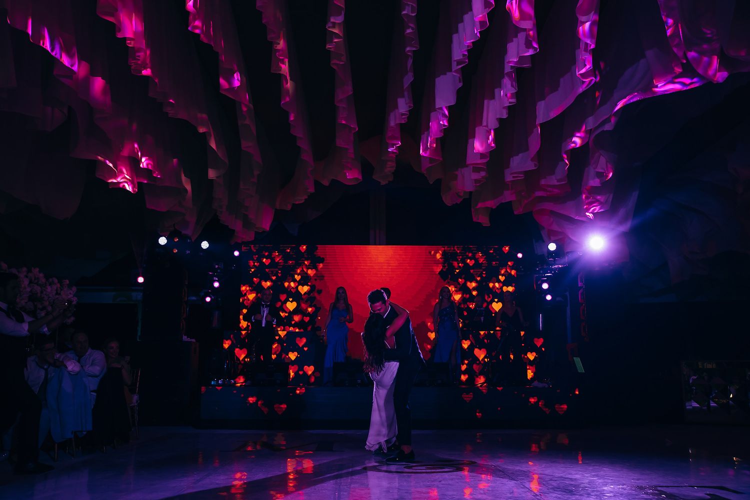Dance floor illuminated with purple and red lighting under decorative hanging installations.
