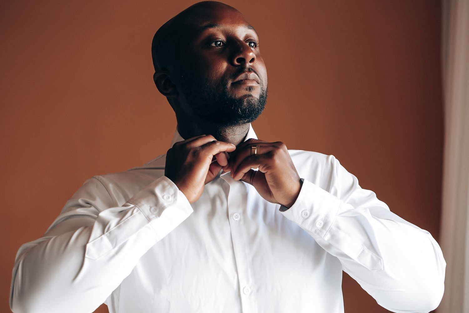 A person adjusts their bowtie while wearing a crisp white dress shirt in a formal setting.