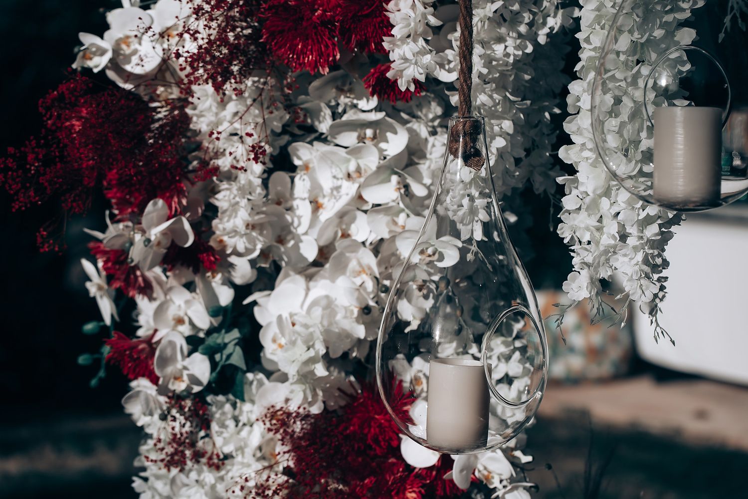 Elegant wedding decor featuring cascading white orchids and deep red flowers with hanging candles in glass holders.