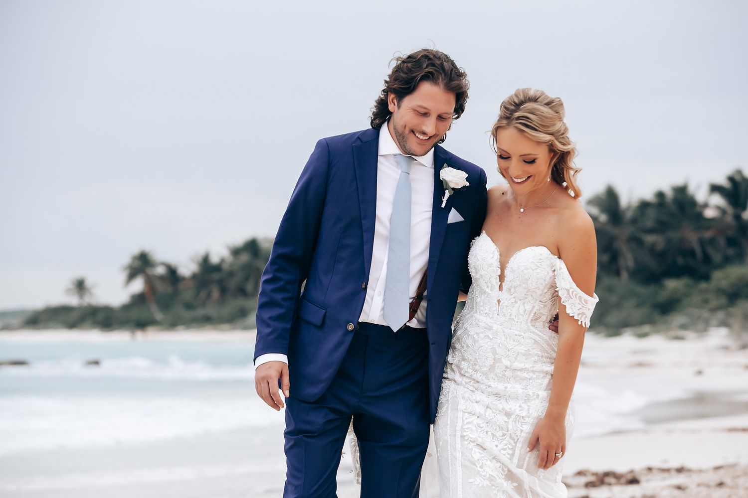Couple sharing intimate moments on a windy beach with ocean backdrop.