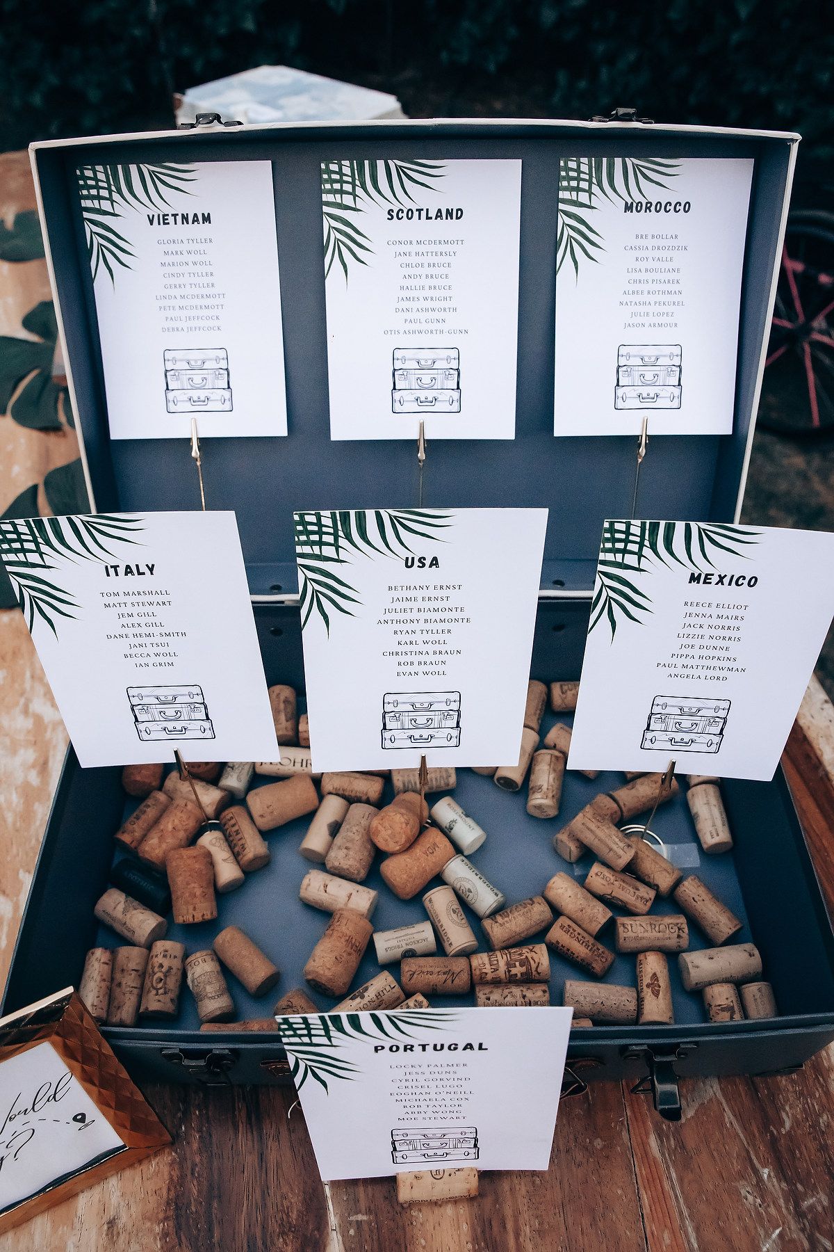 Wedding seating chart display decorated with wine corks and tropical leaf designs.