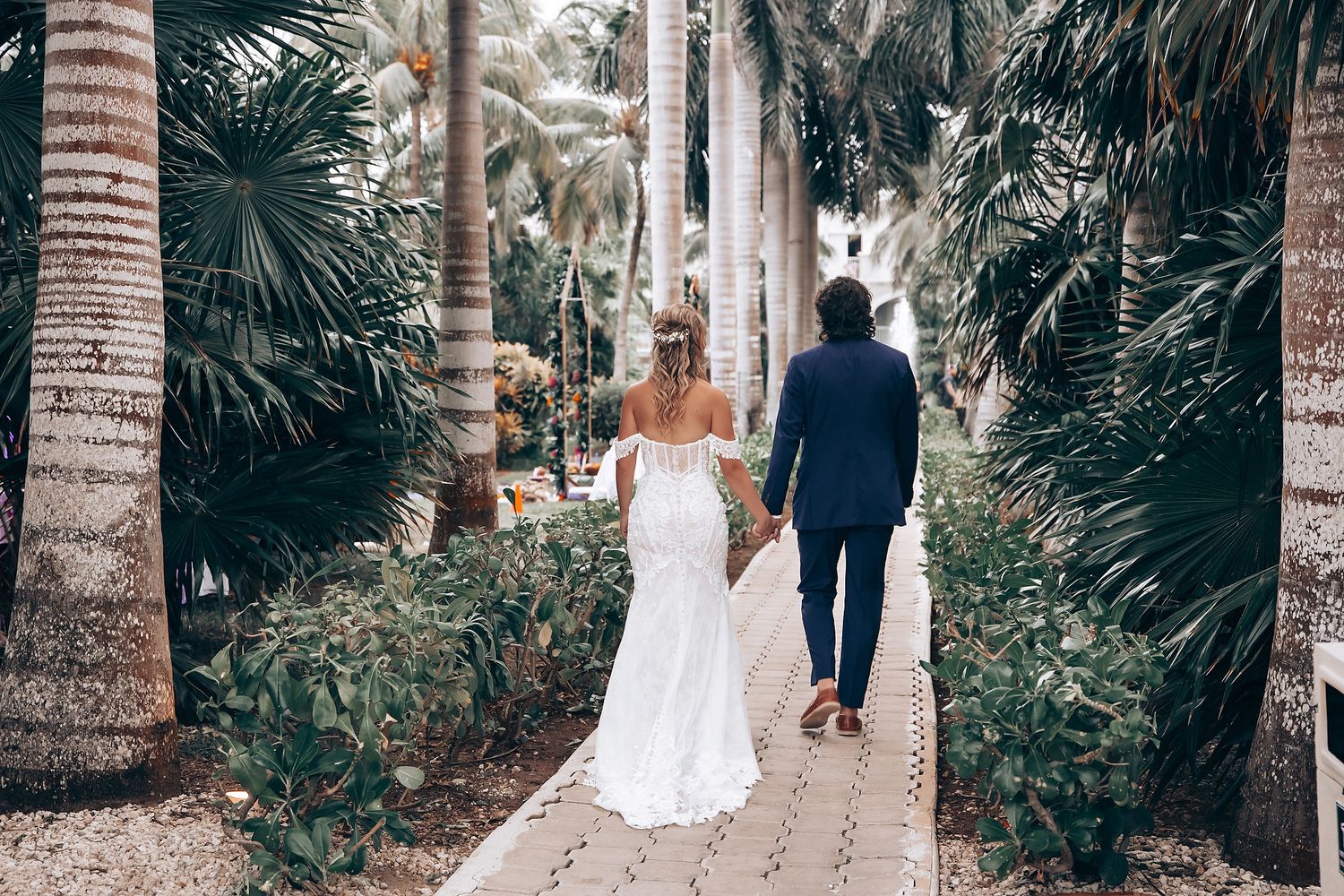 Wedding couple walks down a palm tree-lined path after their ceremony.