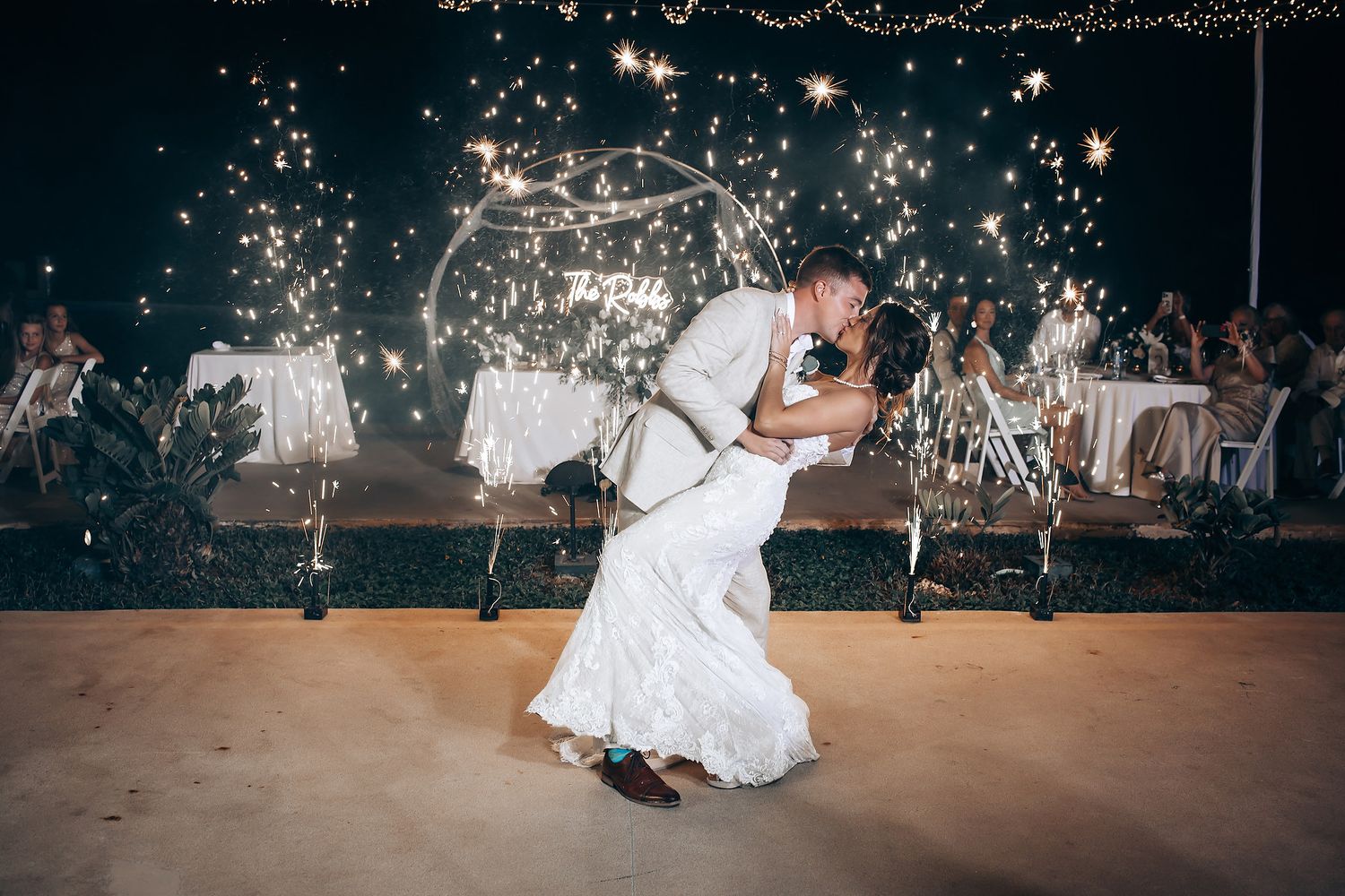 Wedding couple dances under twinkling lights at evening reception.