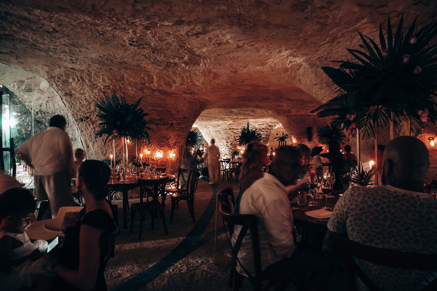 Dimly lit cave venue decorated for wedding reception with warm ambient lighting and palm silhouettes.