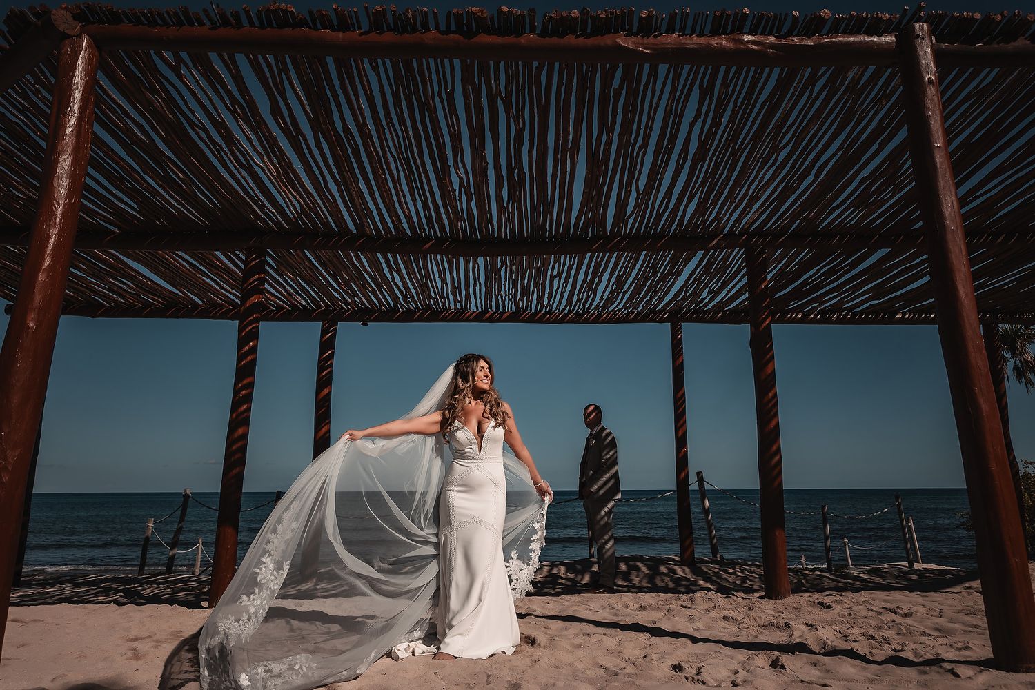 Wedding couple sharing a moment under rustic beach pergola with ocean view.