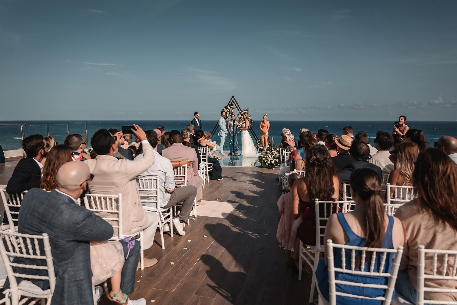 Outdoor wedding reception setup with white chiavari chairs overlooking the ocean.