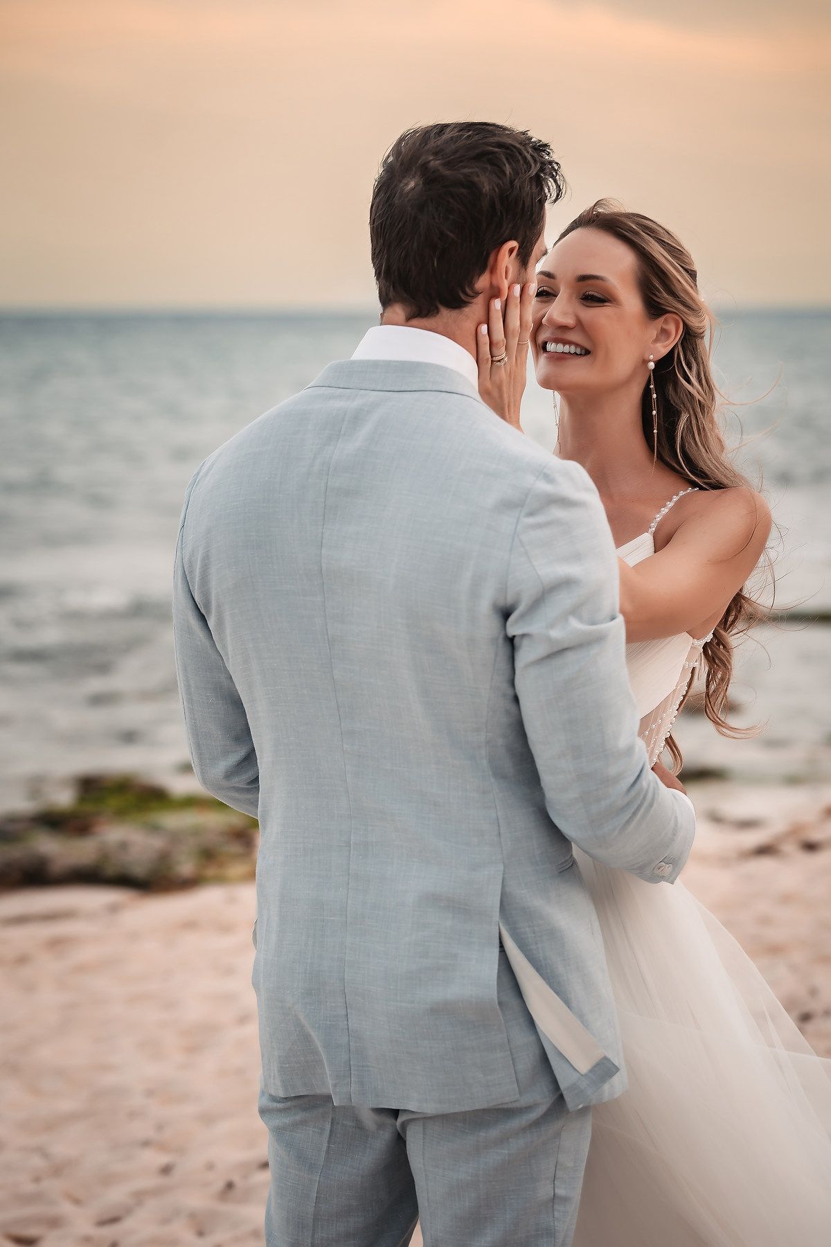 Romantic couple embraces on a beach at sunset with ocean waves in the background.