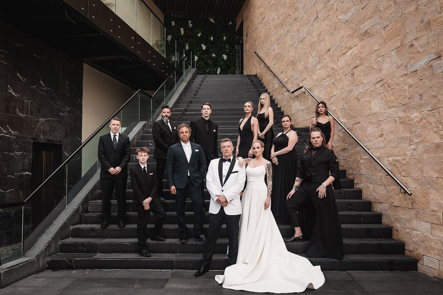 Wedding party poses on dark stone steps against textured stone wall backdrop.