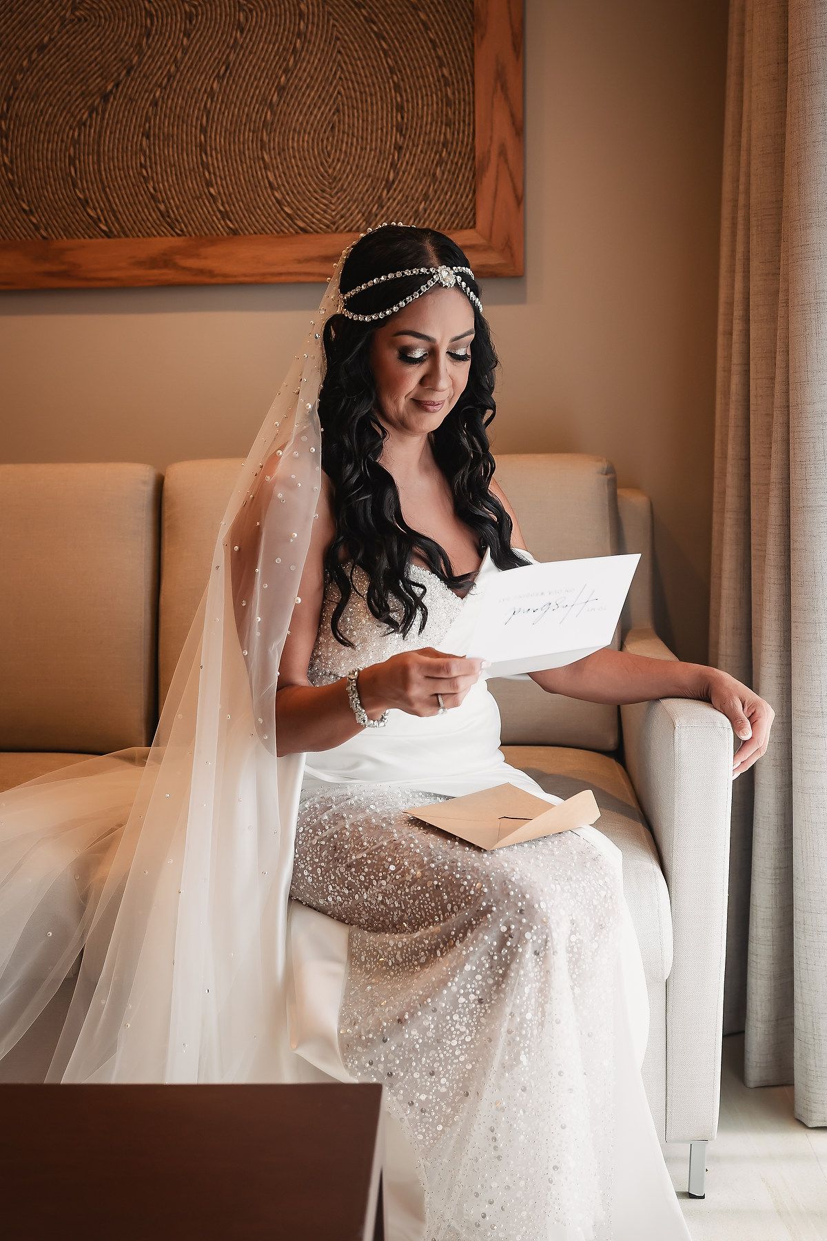 Elegant bride in white dress reading a letter while seated in a chair.