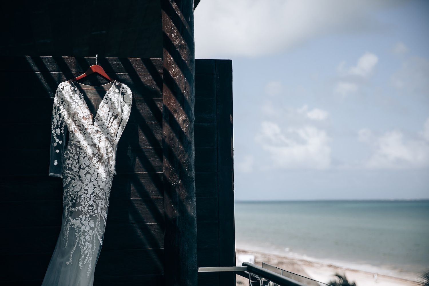 A wedding dress with intricate lace detailing hangs elegantly against a dark background.