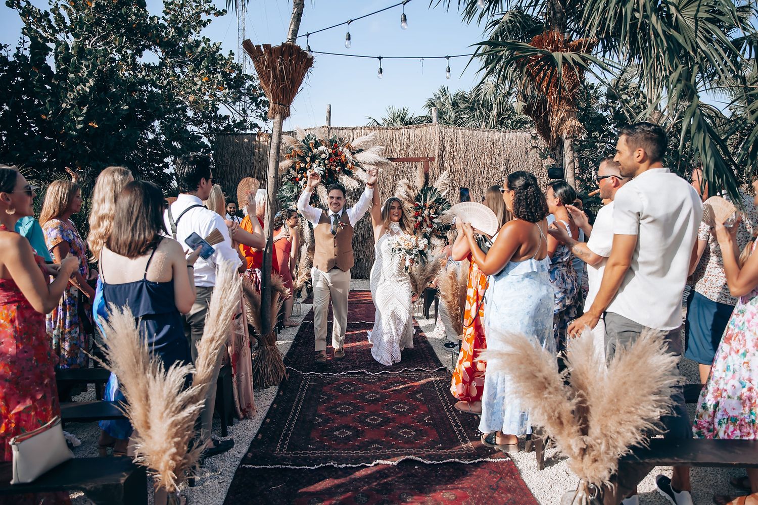 Lively wedding reception with guests dancing under palm trees and festive lighting.