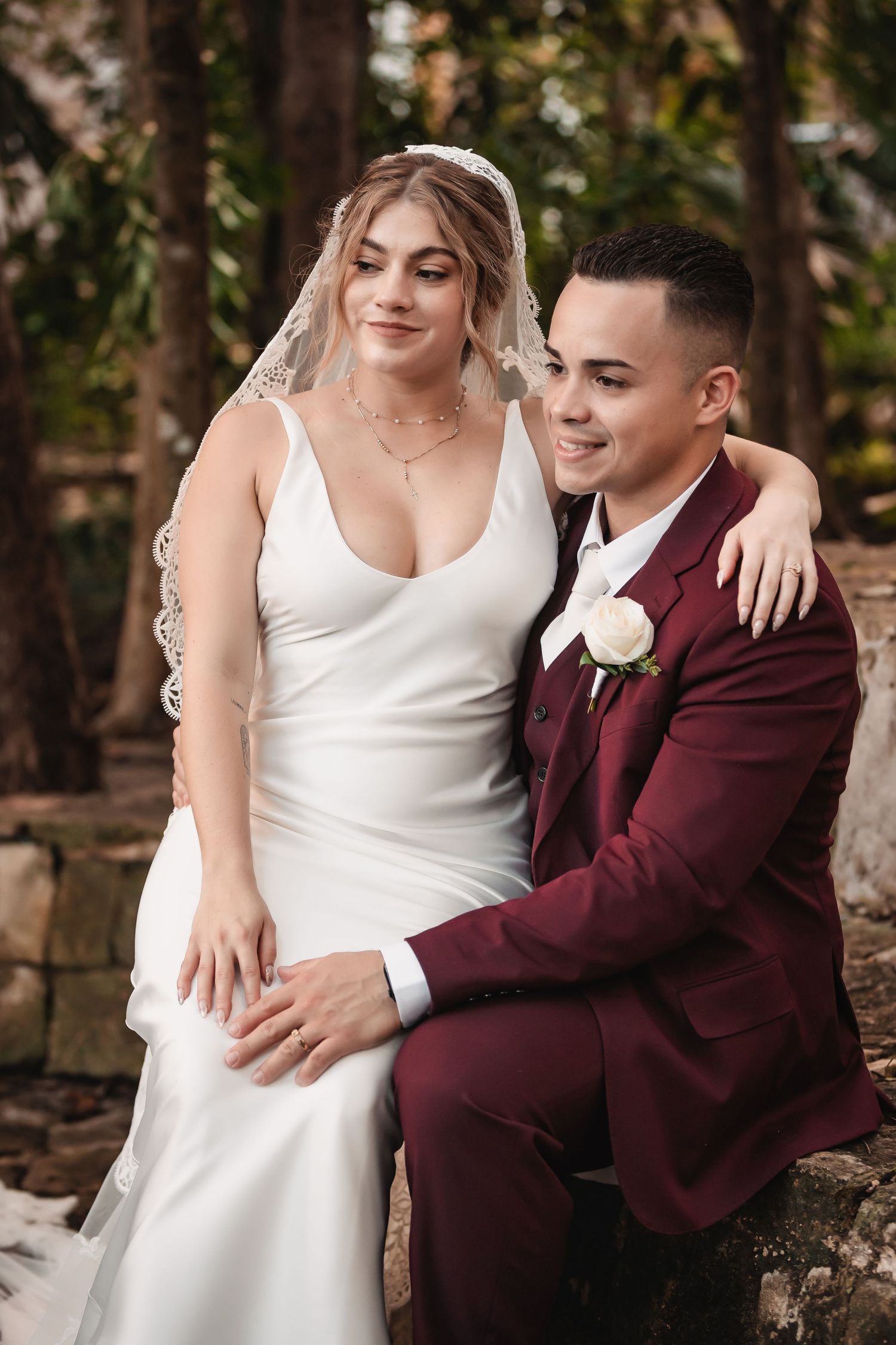 Wedding portrait on stone wall with couple in white dress and burgundy suit.
