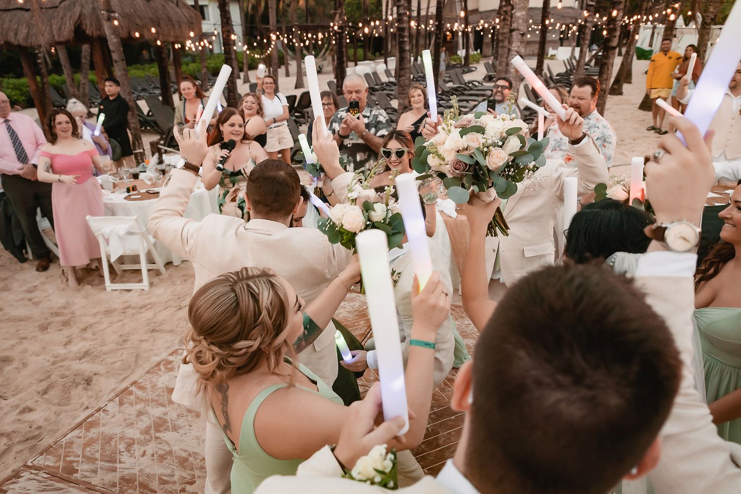 Wedding guests dancing and celebrating at a beach reception under string lights.