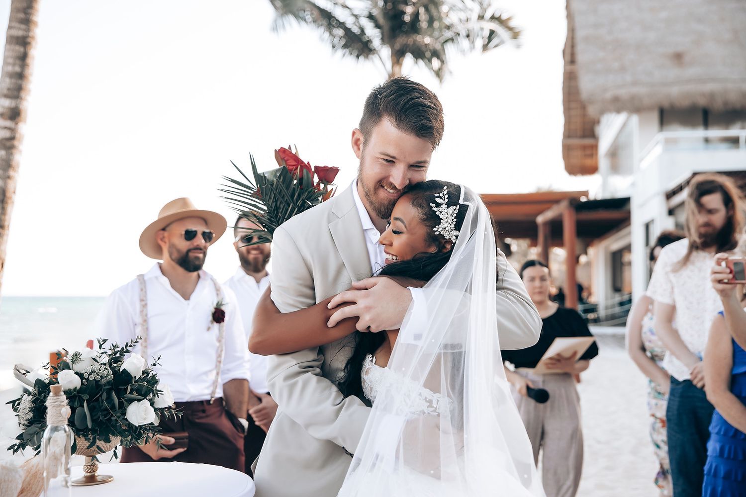 Wedding celebration on a beach with floral arch and guests in attendance.