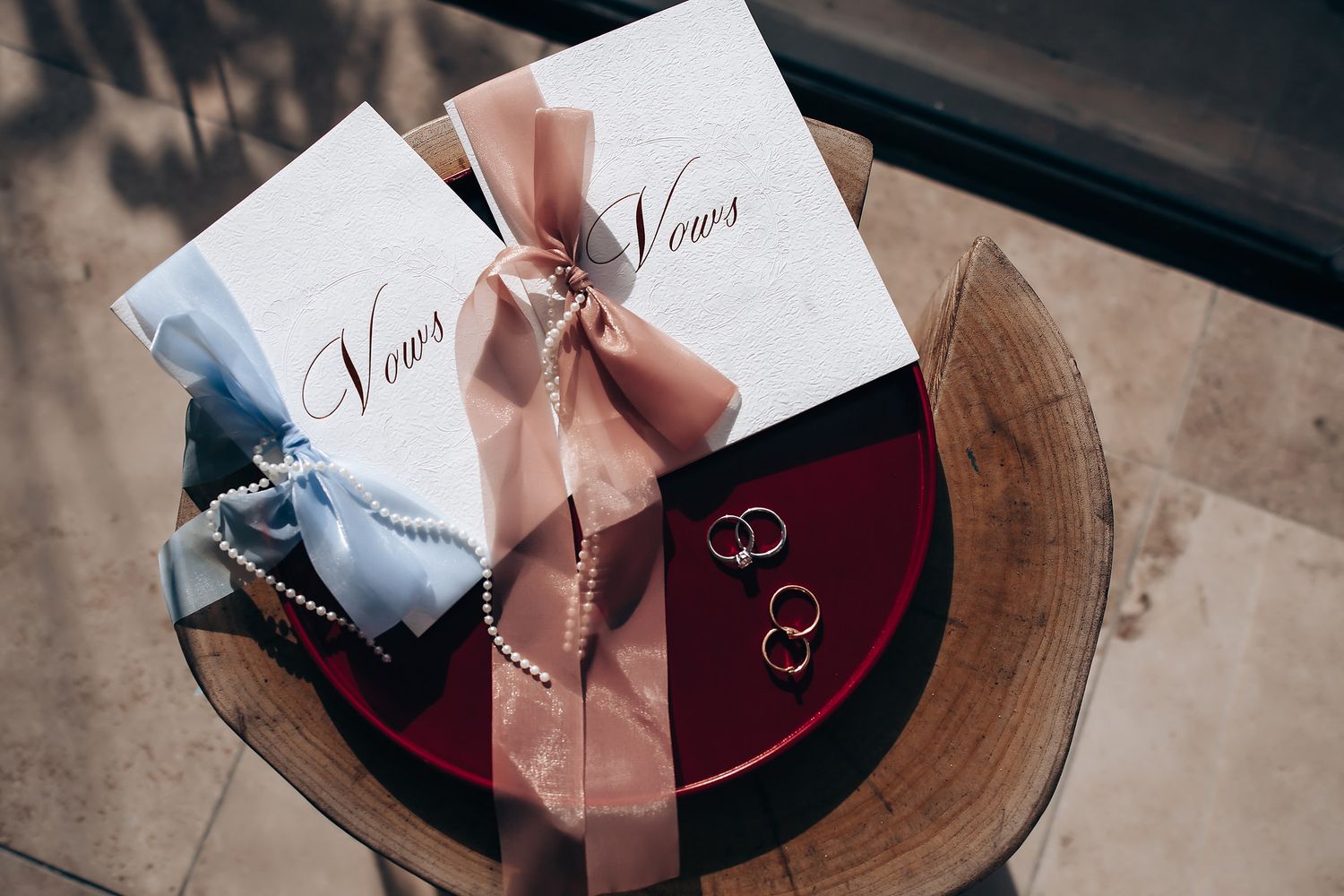 Wedding invitation cards with pink ribbons and wax seals displayed on dark wooden surfaces.