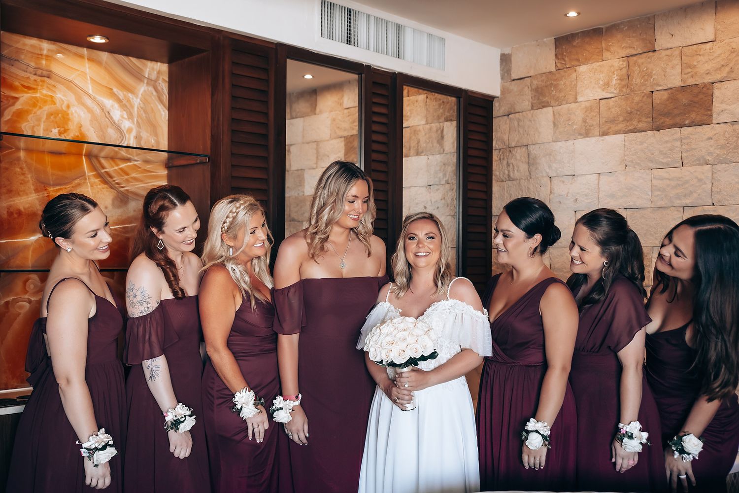 A group in formal attire stands together at a wedding celebration against a stone wall backdrop.