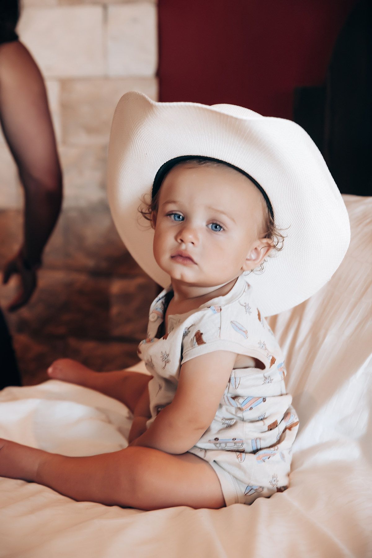 Small child wearing white cowboy hat sitting on white bedding.