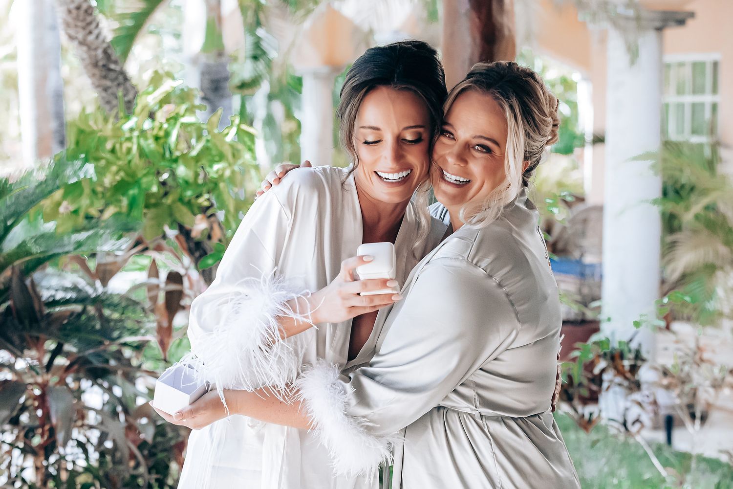 Two people in white robes share a joyful moment together while holding a coffee cup on a sunny patio.