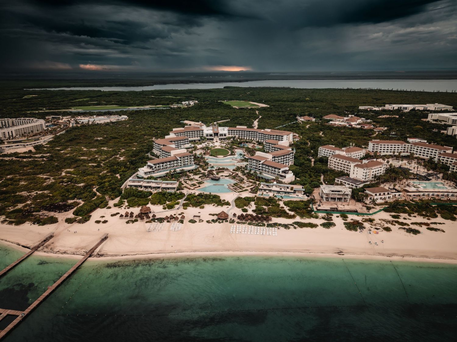 Aerial view of a luxury beachfront resort with turquoise waters under dramatic storm clouds.