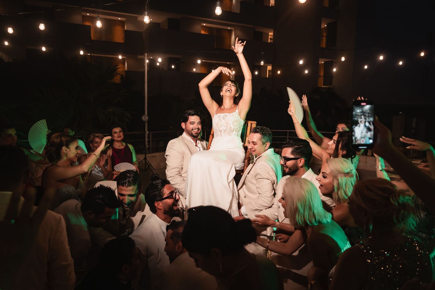 Festive party scene with string lights overhead and dancing crowd in dark venue.