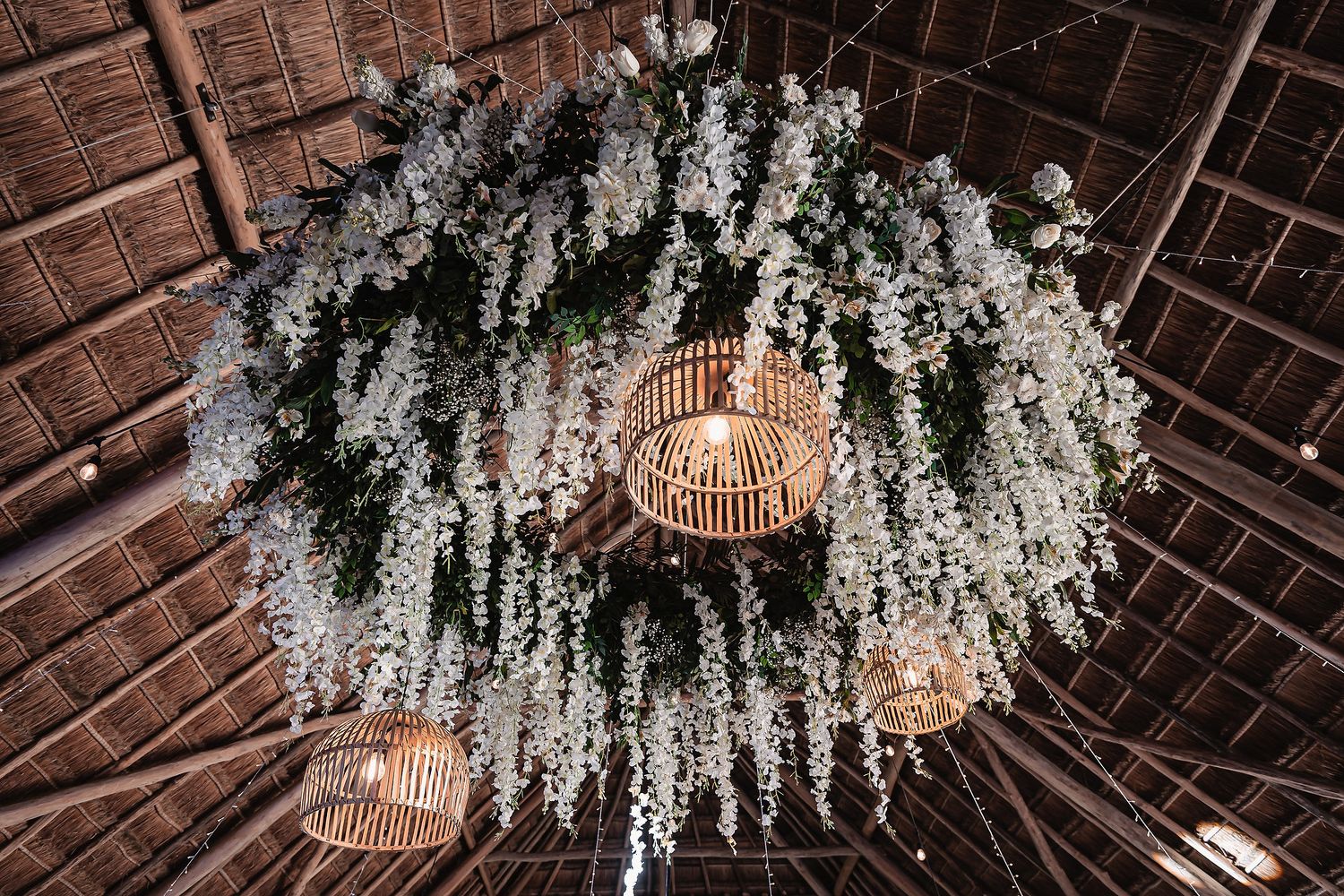 Elegant white floral arrangements hang from wooden beams creating a stunning ceiling installation.