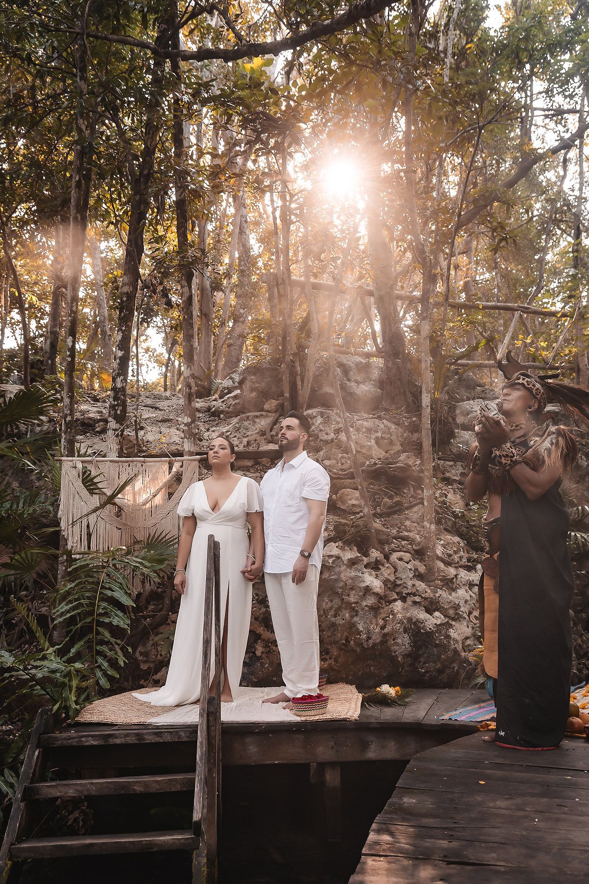 Sunlit outdoor wedding ceremony with traditional Mayan officiant in natural stone setting.