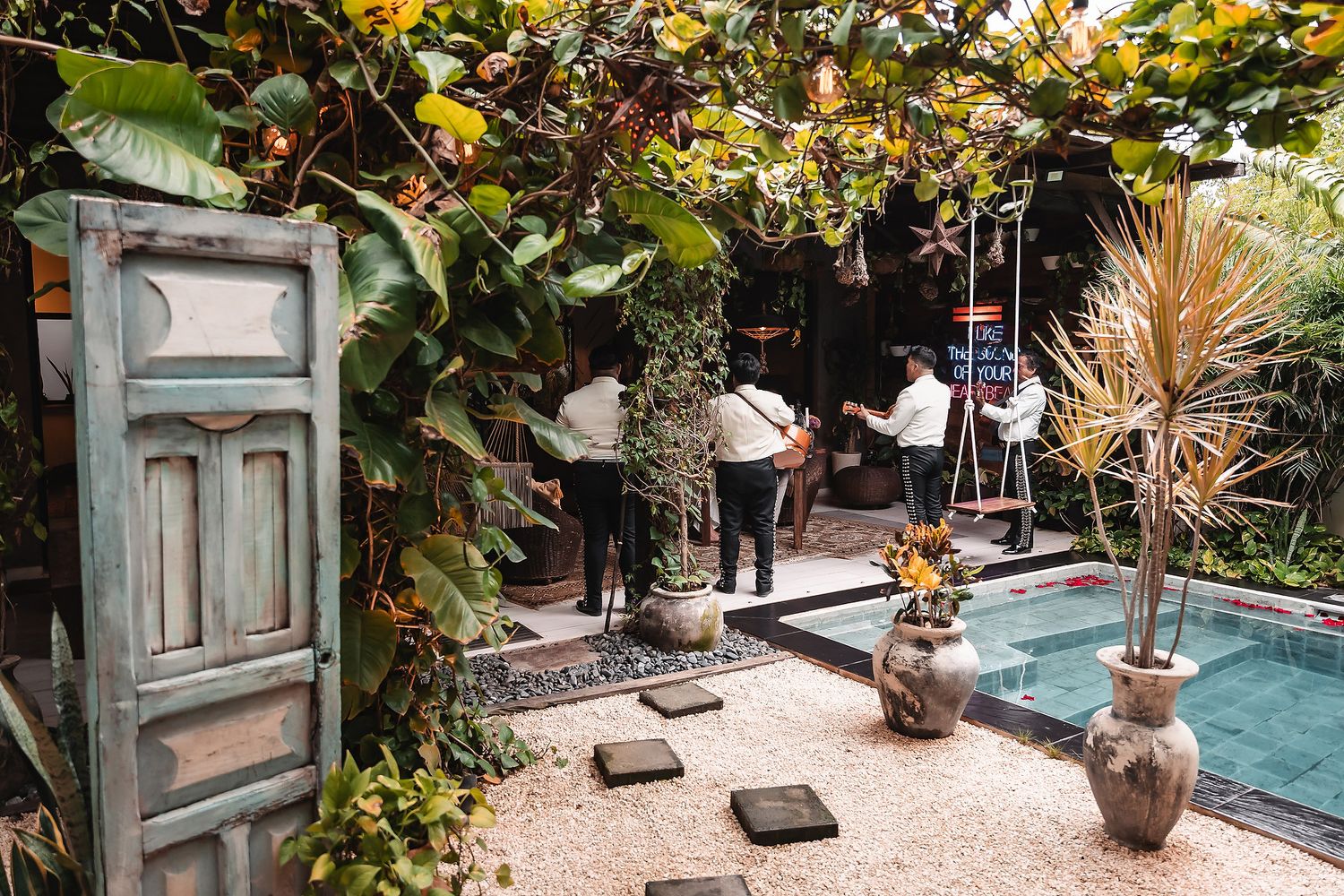 Musicians performing by pool area with vintage door and tropical garden setting.