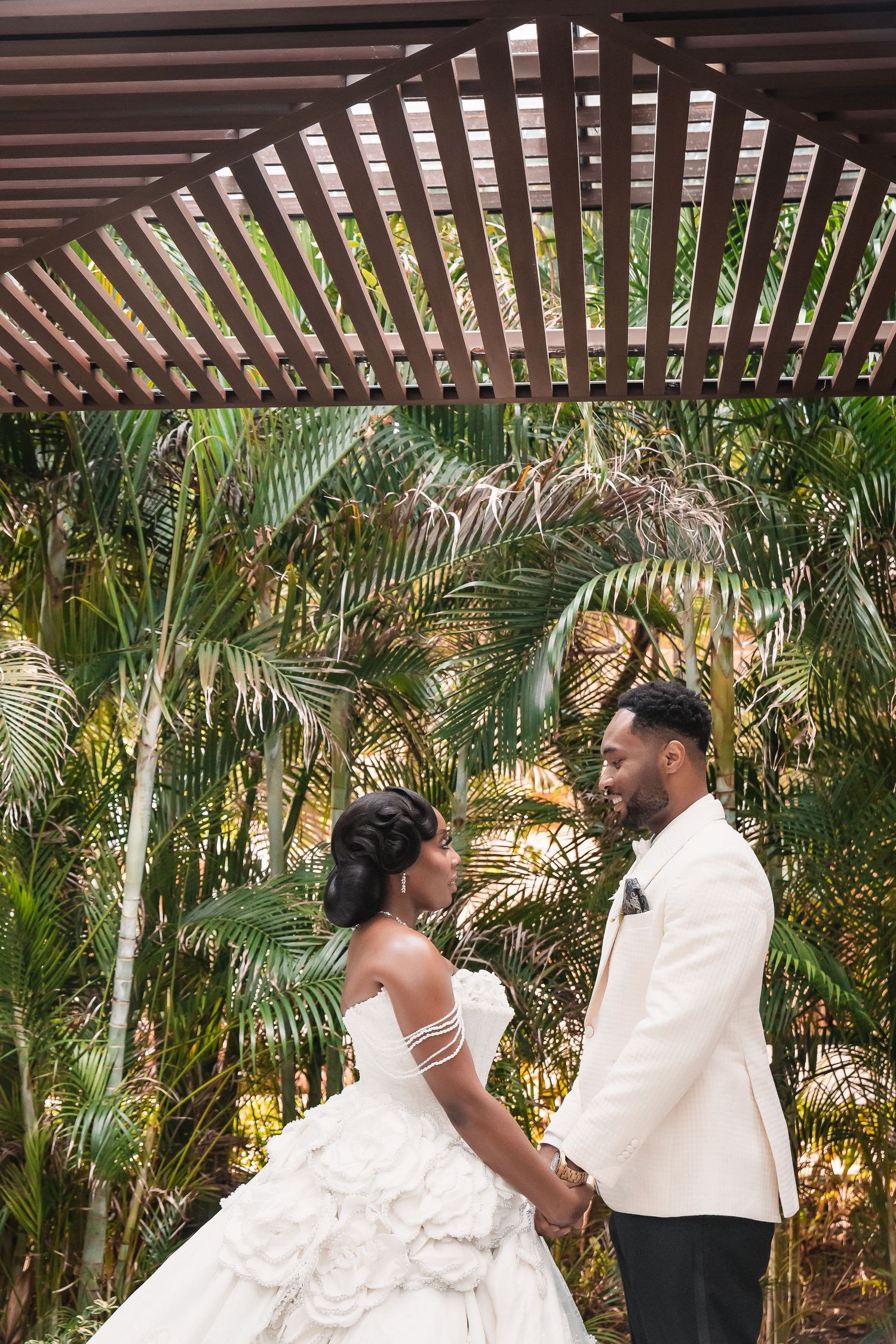 A couple shares joyful moments under a wooden pergola surrounded by tropical palms.