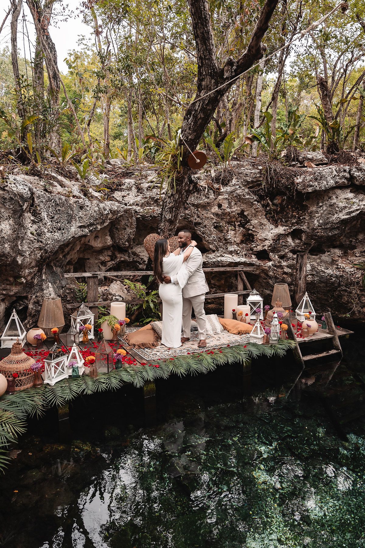 Romantic proposal setup on a rocky ledge overlooking a crystal-clear cenote with decorative lanterns.