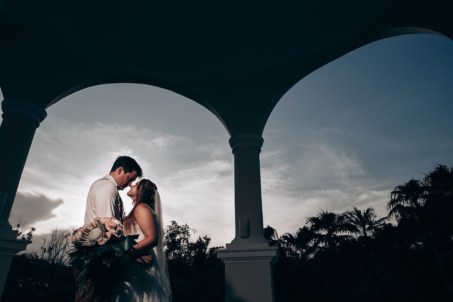 Romantic silhouettes captured through architectural arches at sunset.