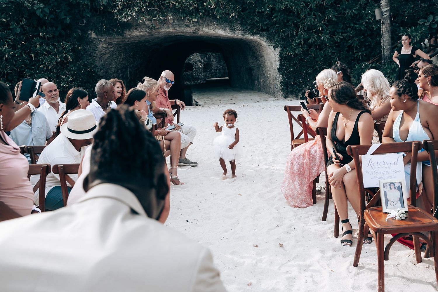 Wedding guests watch as a small child walks down the aisle at a beach ceremony.