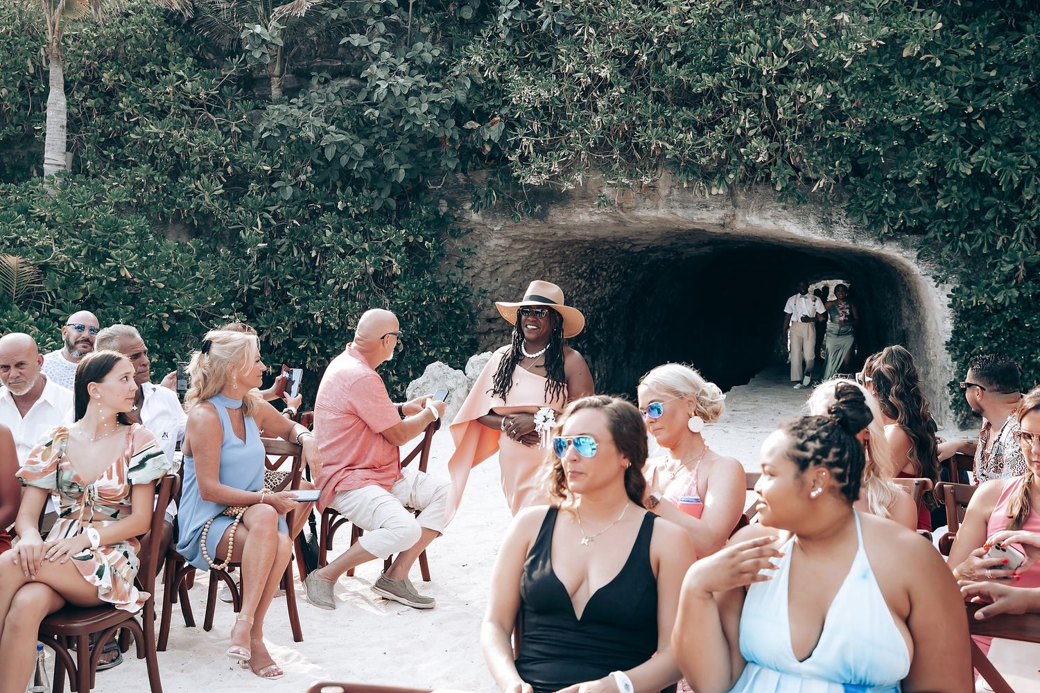 Wedding guests seated in white chairs on a tropical beach for an outdoor ceremony.
