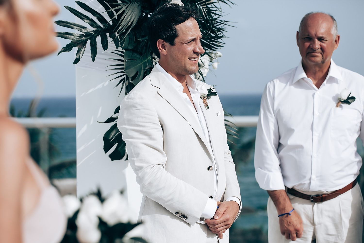 Beachside wedding ceremony with tropical palm decor and white attire.