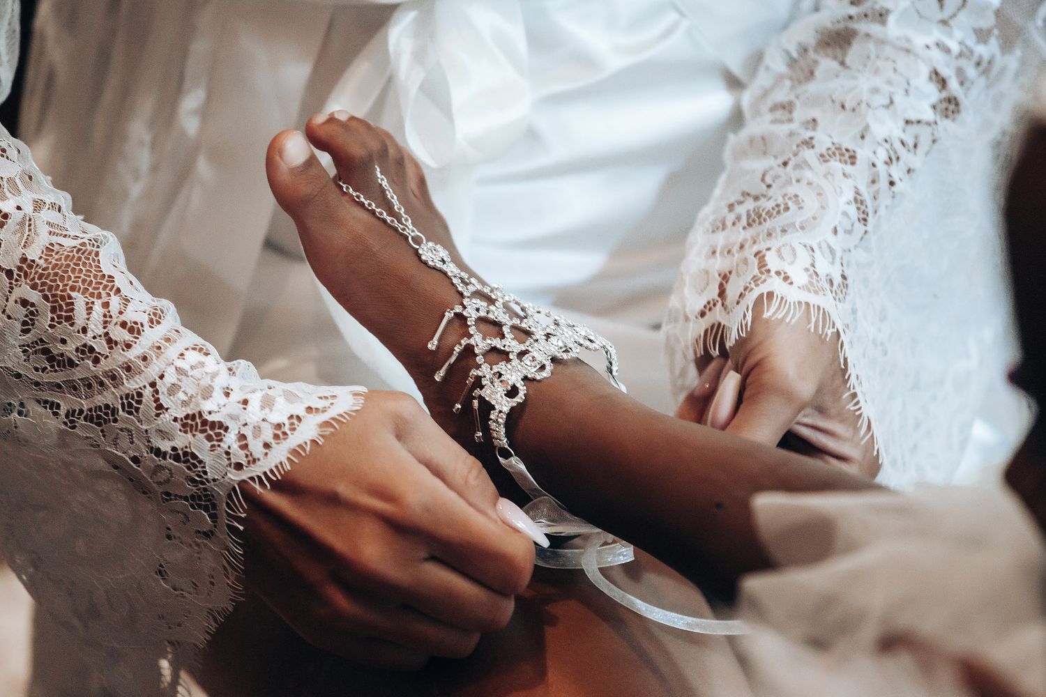 Close-up view of hands adjusting lace details on an elegant white wedding dress sleeve.