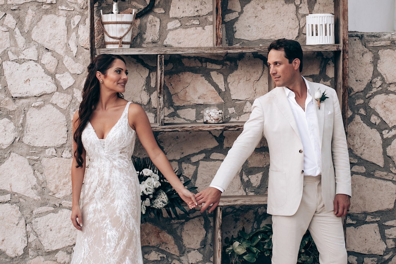 Bride and groom share intimate moments against stone architecture in elegant white wedding attire.